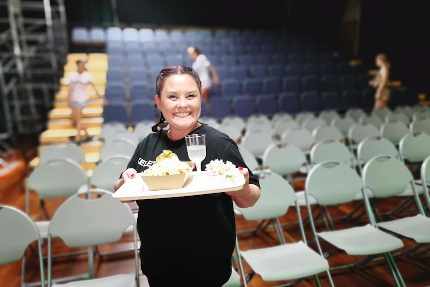 A woman carrying a tray with drinks and food on it smiles.