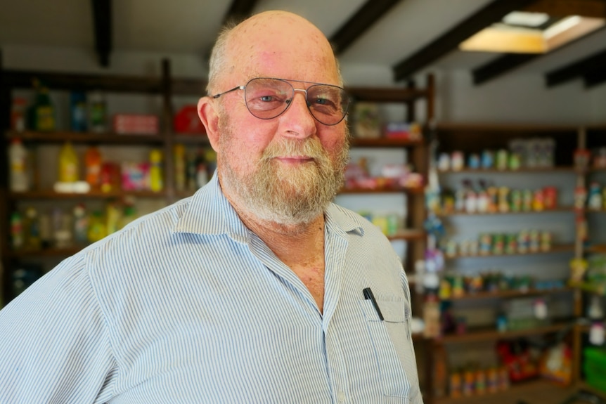 A man with glasses stands inside a small store.