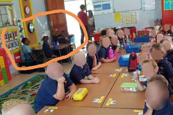 Children sitting in a classroom, faces blurred, separated by race