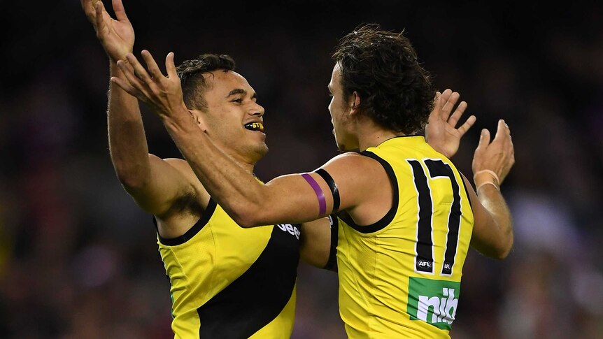 Two AFL teammates celebrate a goal.