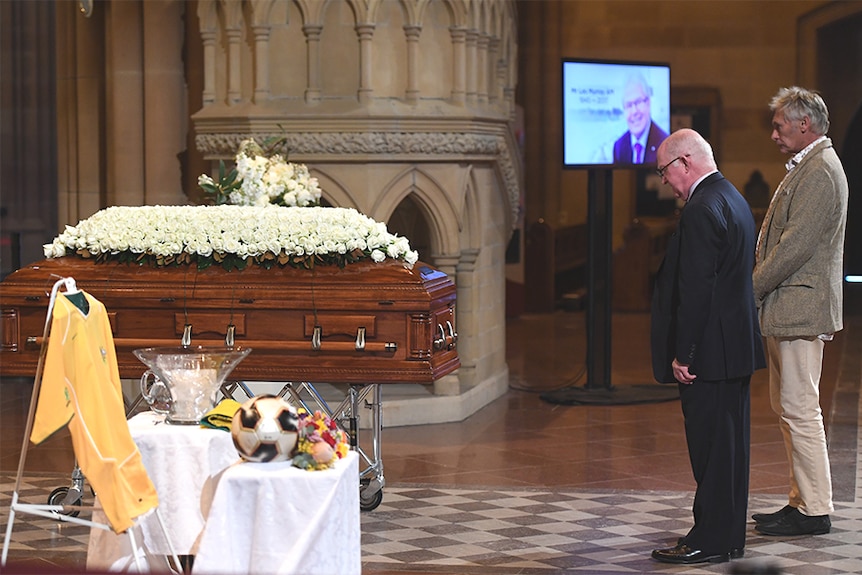 Two men standing at a coffin.