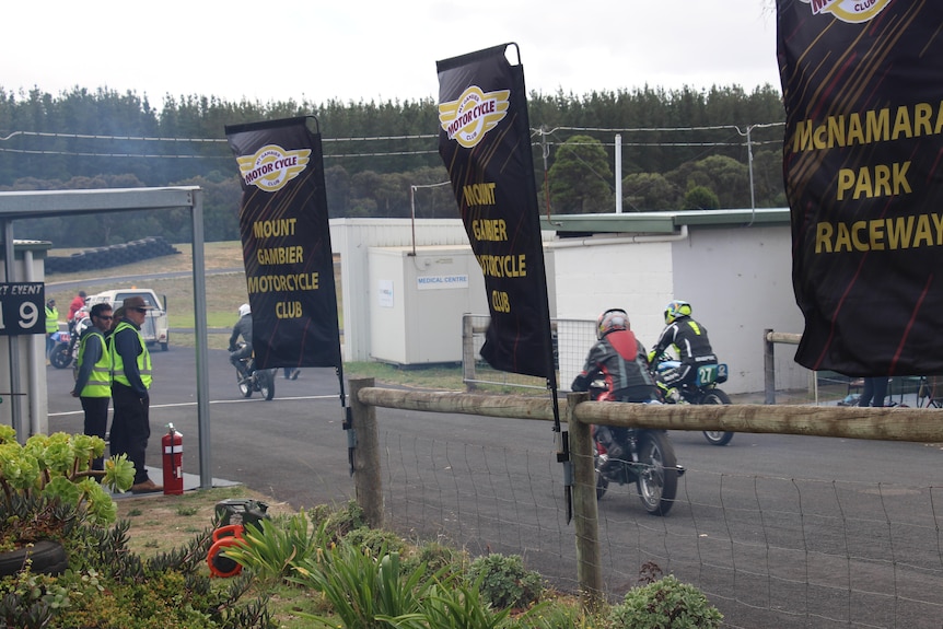 Motorbike racers on a track with flags on the side of the fence 