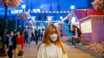 A young woman in a face mask walks through a street strung with fairy lights in Seoul.
