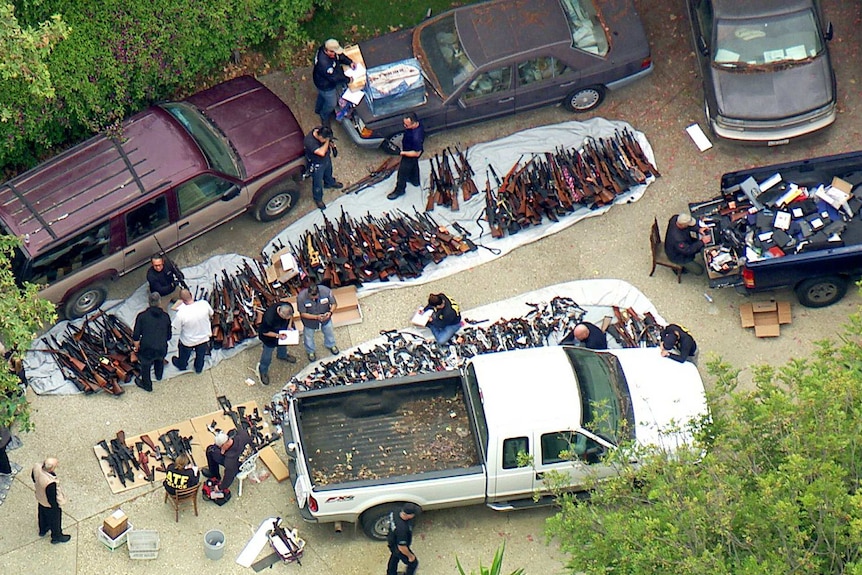 A huge stash of guns and ammunition is laid out on a driveway between five vehicles while being catalogued.