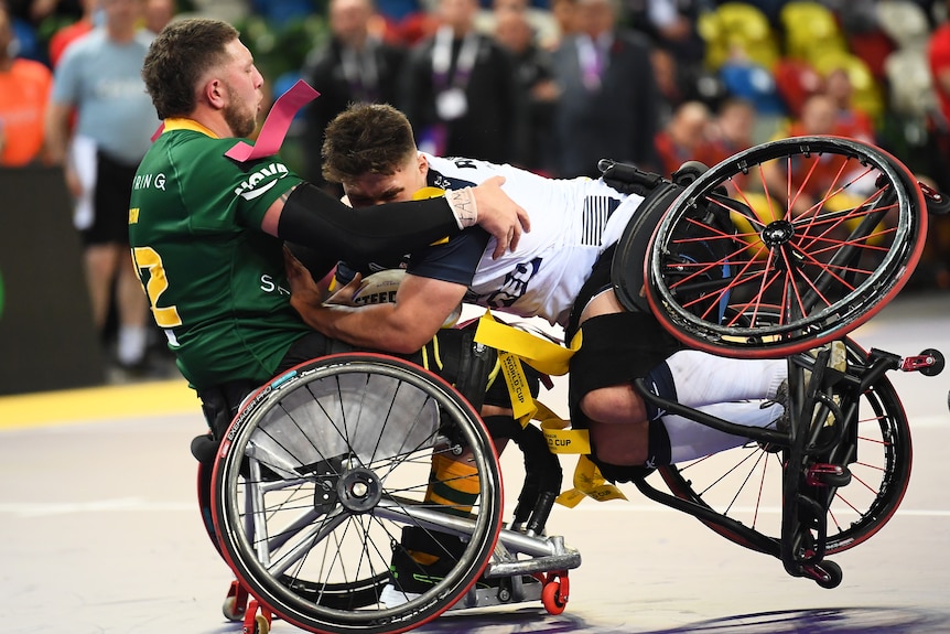 Seorang pemain liga rugby kursi roda Australia meringis saat dia menekel pemain Inggris yang melindungi bola saat dia kehilangan keseimbangan.