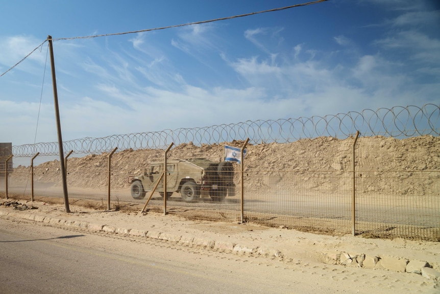 A tank drives past a wire fence 