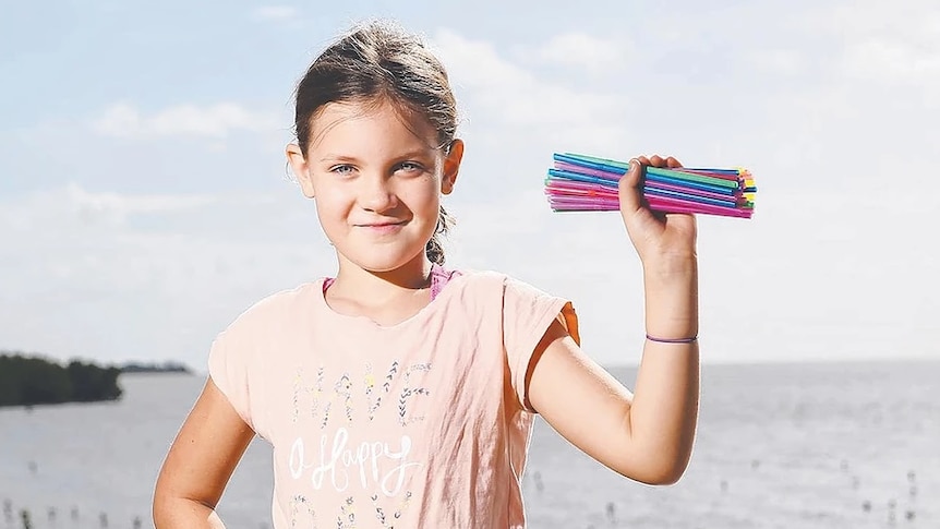 10-year-old girl on a beach holds straws in hand.