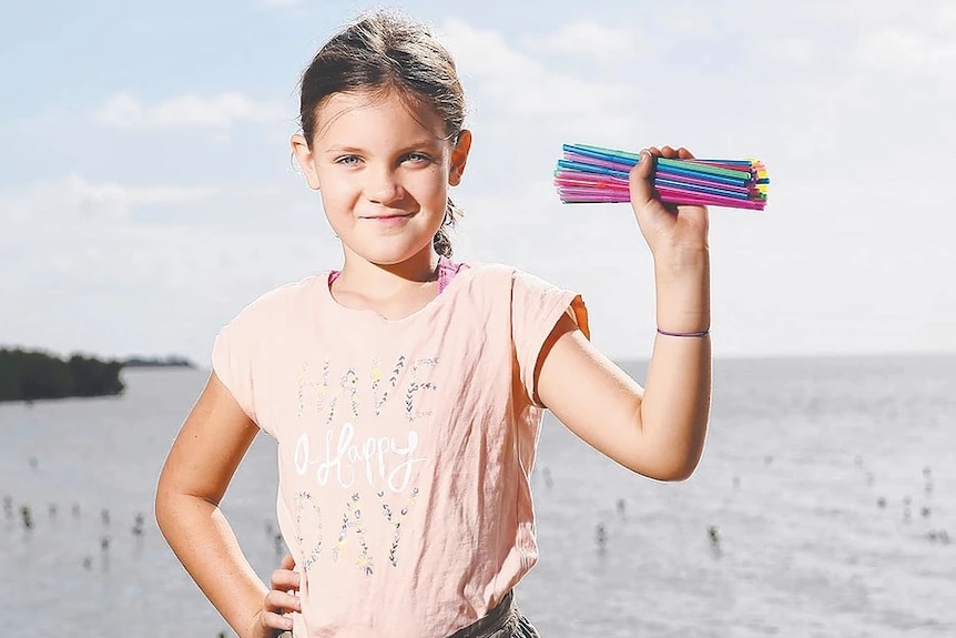 10-year-old girl on a beach holds straws in hand.