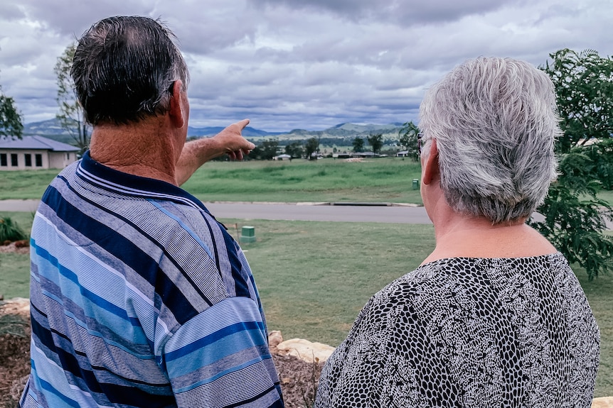 a couple stand in their front yard looking over a valley