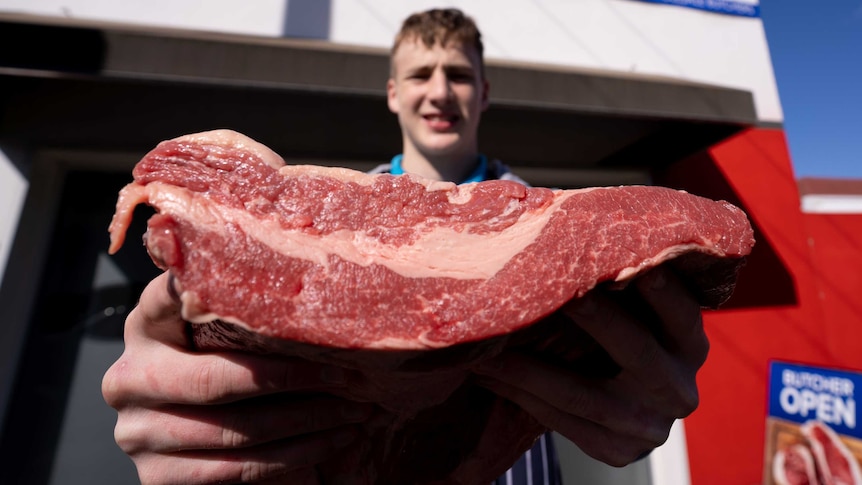 Young apprentice Toby holds out a big cut of brisket outside the Mount Gambier butcher he works at.