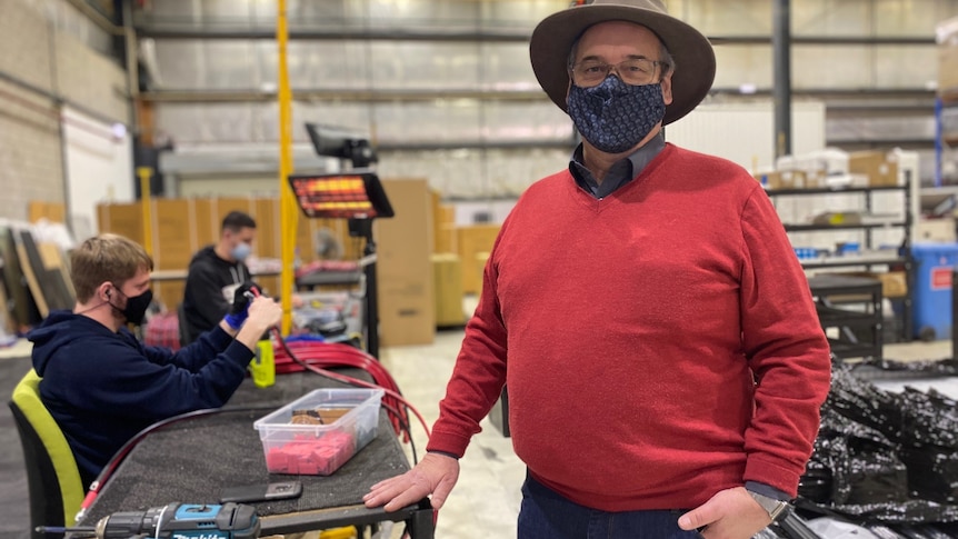 a man staring at the camera smiling in a covid mask in a battery factory