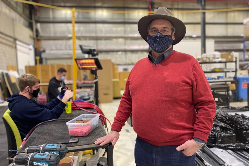 a man staring at the camera smiling in a covid mask in a battery factory