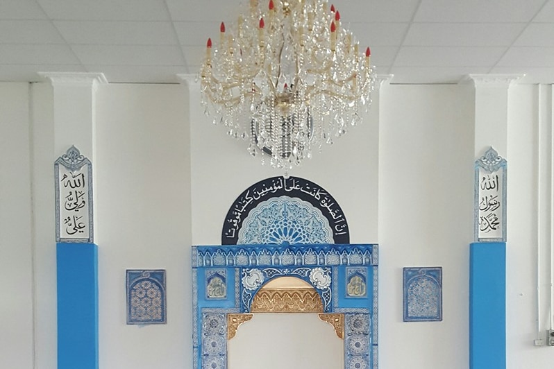 A view from inside the mosque with blue, white and black Arabic scripture and a chandelier in view. 