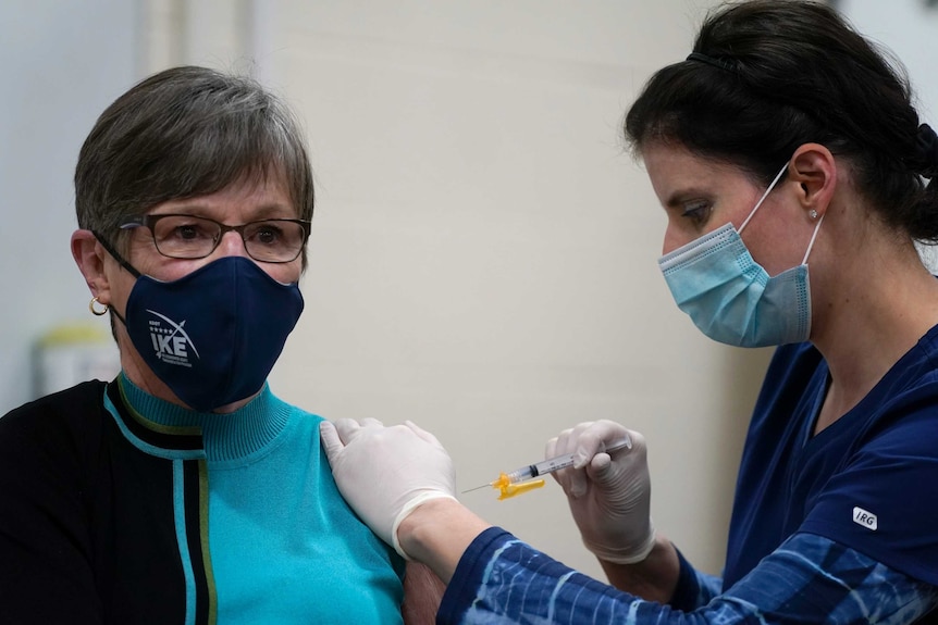 A public health nurse gives a COVID-19 vaccine injection to an older woman.