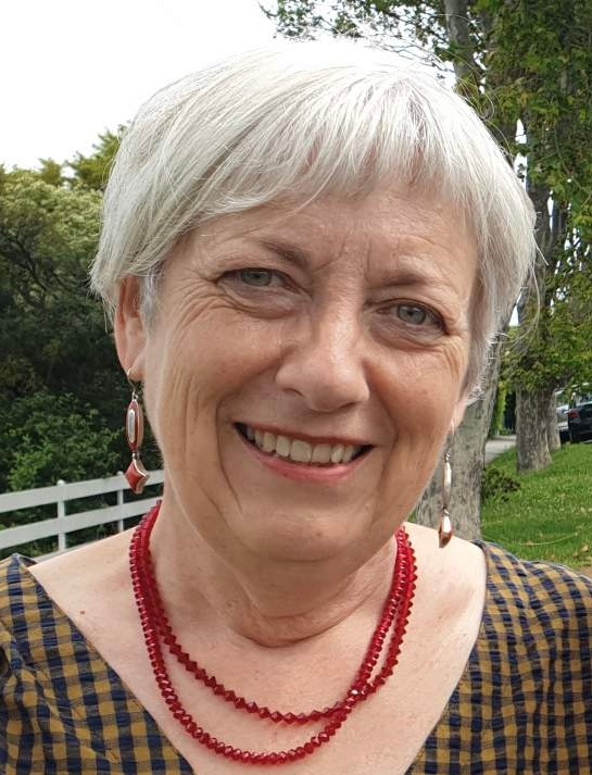 Una mujer con el pelo blanco muy corto y un collar rojo sonríe.