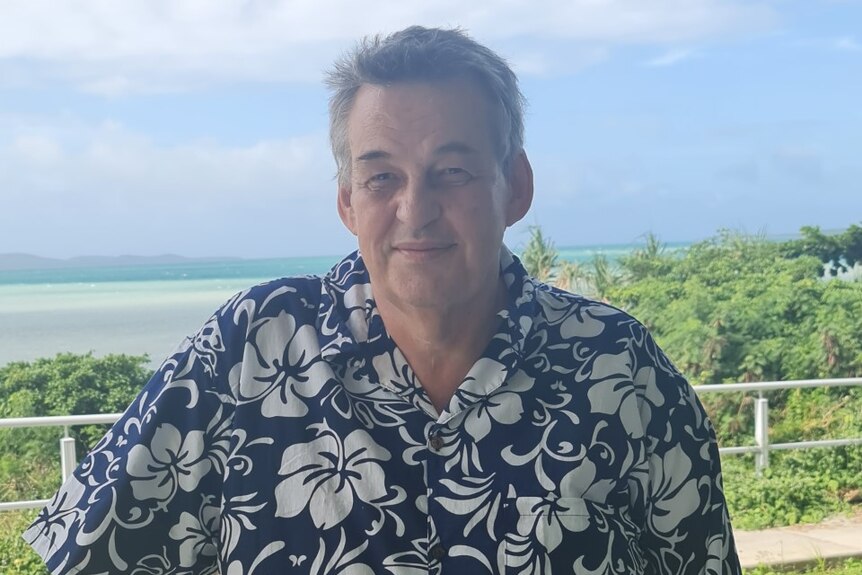 Nick McGregor in a floral-printed shirt smiling in front of a beach