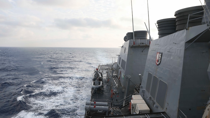 A view of a navy ship with wake left in the ocean visible.