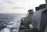 A view of a navy ship with wake left in the ocean visible.