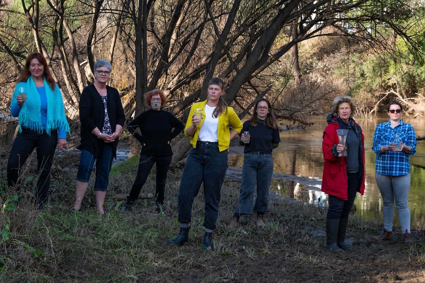 A group of environmentalists stand next to a river holding glasses of water
