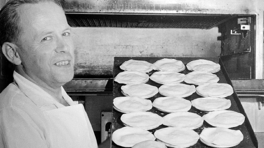 Pastry cook holds a tray of Australian meat pies