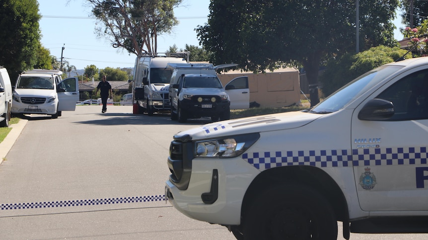 A photo of the front of a police car with police cars and officers in the background.