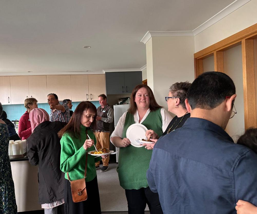 Hay gente parada en una cocina, algunas comiendo en platos de papel.