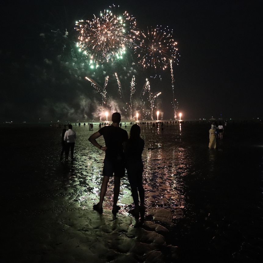 Two people watch fireworks at a beach