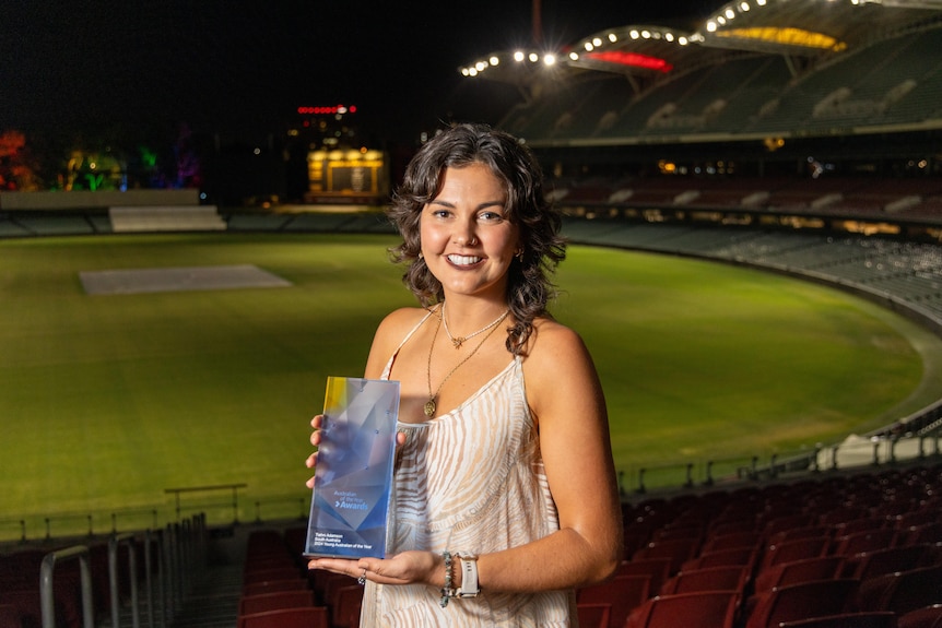 A woman holding a blue glass award in the stands overlooking an oval