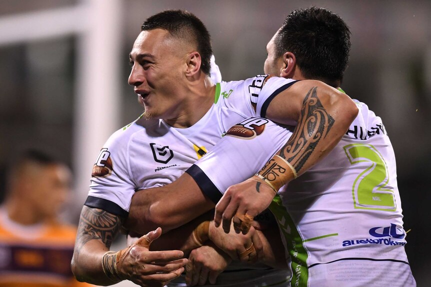 A Canberra Raiders NRL smiles as he celebrates a try with two teammates against the Brisbane Broncos.