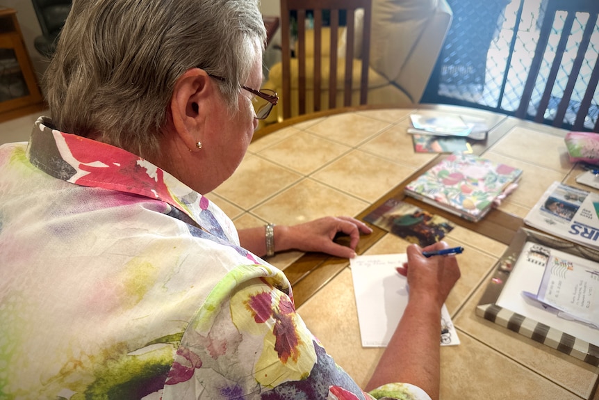 A smiling woman hands writes a letter at a table