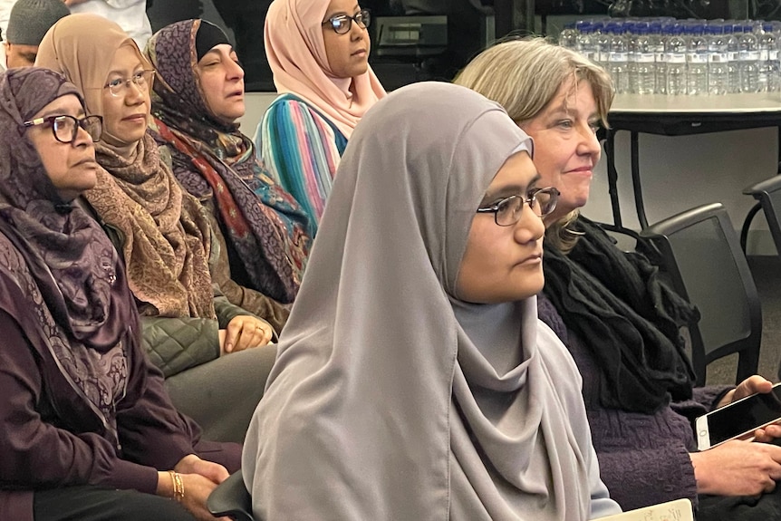 A group of women in headscarves sit in an audience at a community event. 