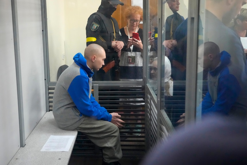 A Russian soldier sits behind glass in a court room