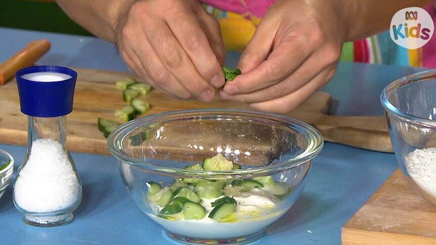 Breaking up mint into a bowl which contains yoghurt and cucumber