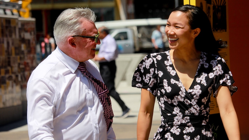 A man and a woman in a street smile at each other