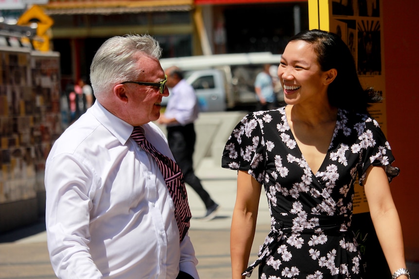 A man and a woman in a street smile at each other