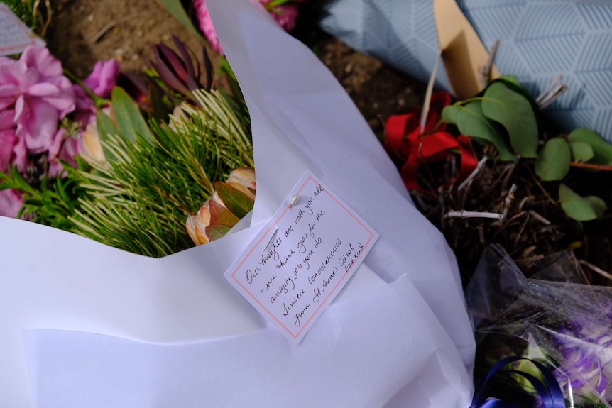 A close up shot of a bouquet of flowers with a condolence note pinned to it.