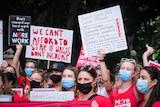People wearing masks hold protest signs