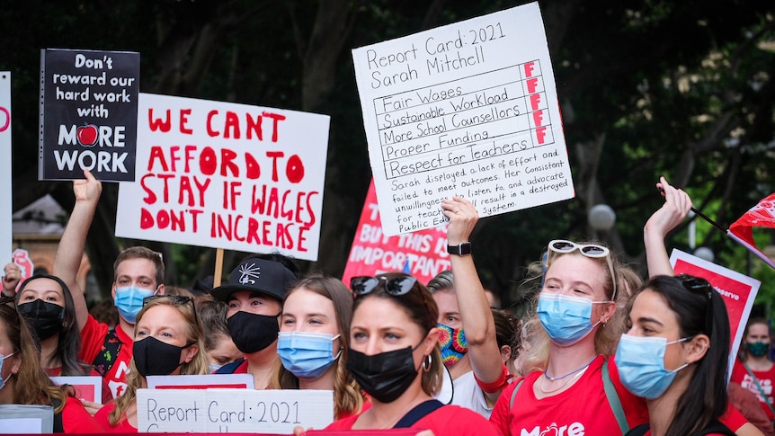 Teachers wearing masks hold protest signs