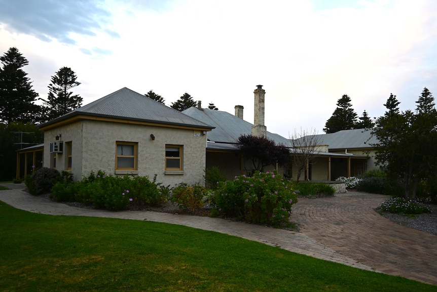 A stone house surrounded by bushes with a paved pathway