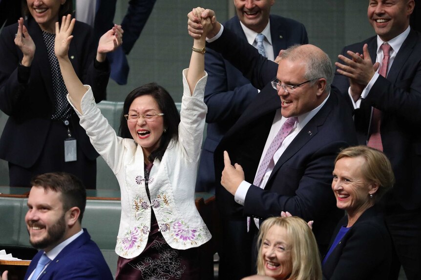 Scott Morrison 将 Gladys Liu 的手举在空中，另一只手向她展示。 后面的议员们笑着鼓掌