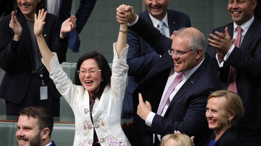 Scott Morrison holds Gladys Liu's arm in the air as he points to her with his other hand. MPs behind are smiling and clapping