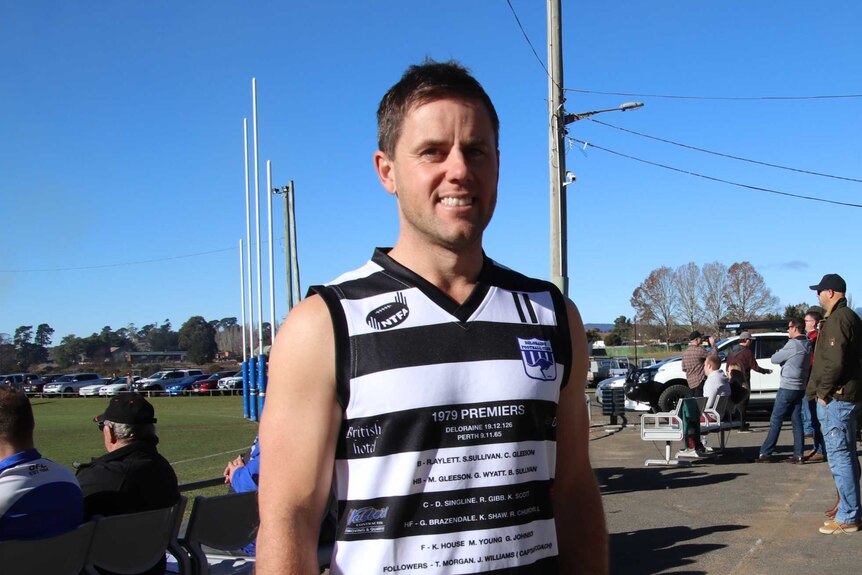 A football player stands at the clubhouse wearing a striped black and white top.