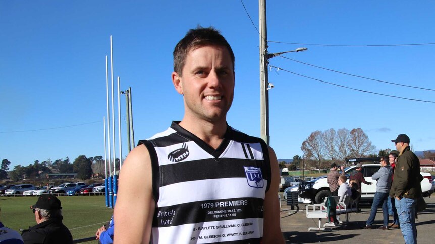 A football player stands at the clubhouse wearing a striped black and white top.