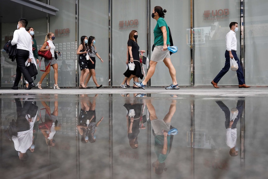 Gli impiegati che indossano maschere protettive camminano nel quartiere centrale degli affari di Singapore.