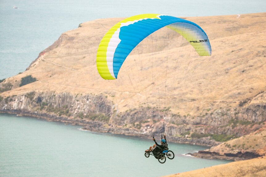 A man in a weelchair paragliding over the ocean and coastline