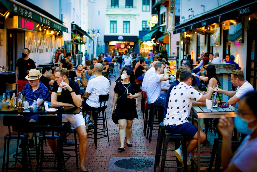 A woman in a mask walks between rows of crowded outdoor tables 