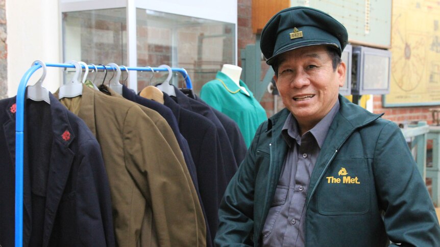 A smiling man wearing an old green tram conductor jacket and cap looks through other old uniforms at the Melbourne Tram Museum