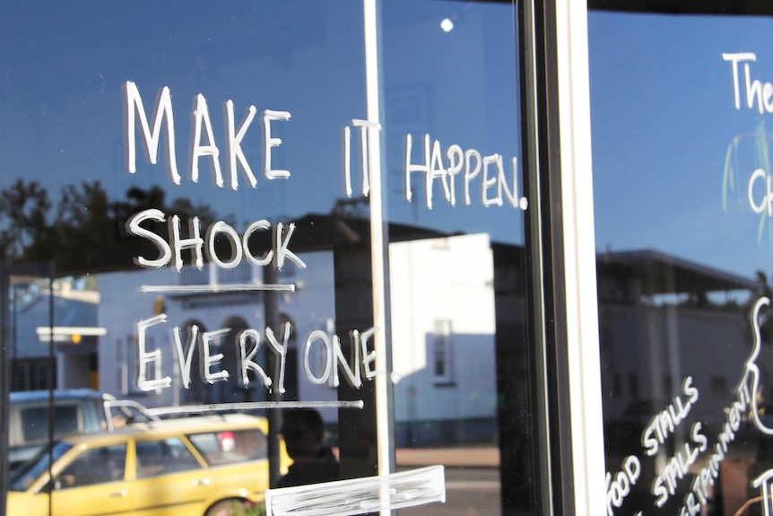 White writing saying 'Make it happen. Shock everyone!' on a glass window.