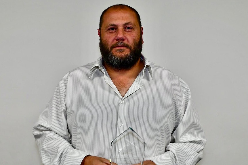 A man wearing a white shirt, holding an award. 