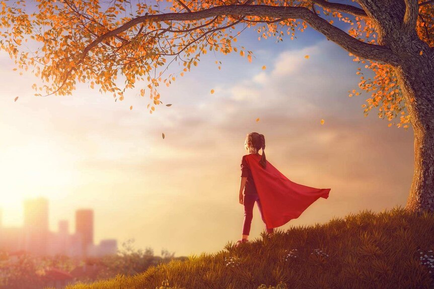 A girl in a cape stands facing towards a distant city.
